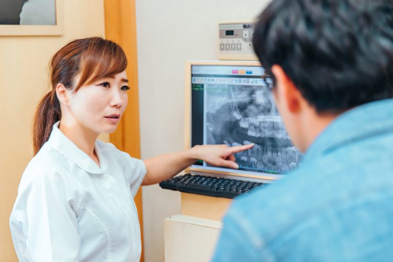 歯のレントゲン写真を使って説明する歯科助手